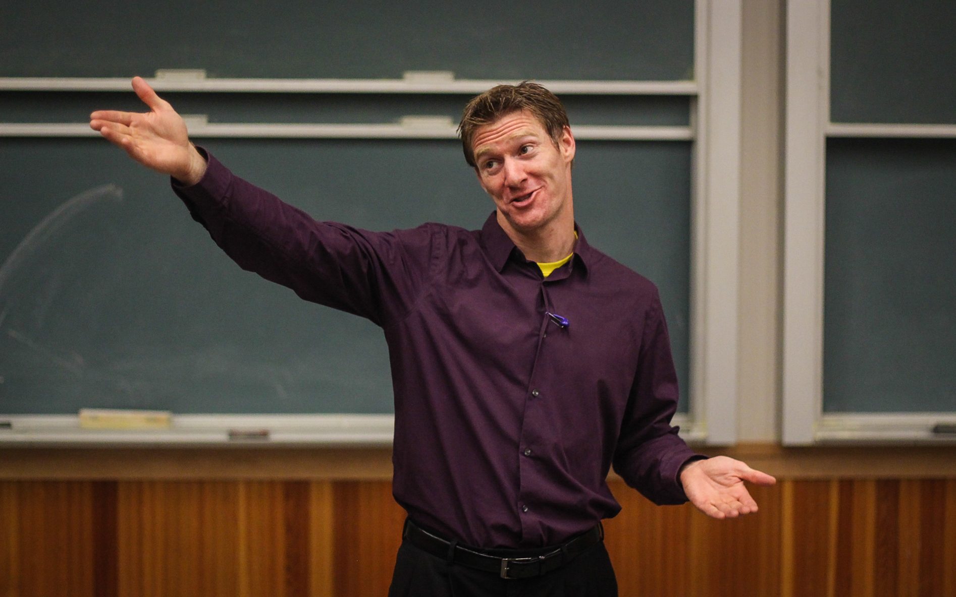 Jared Hippler mid-talk in front of a chalkboard, arms wide, working the room